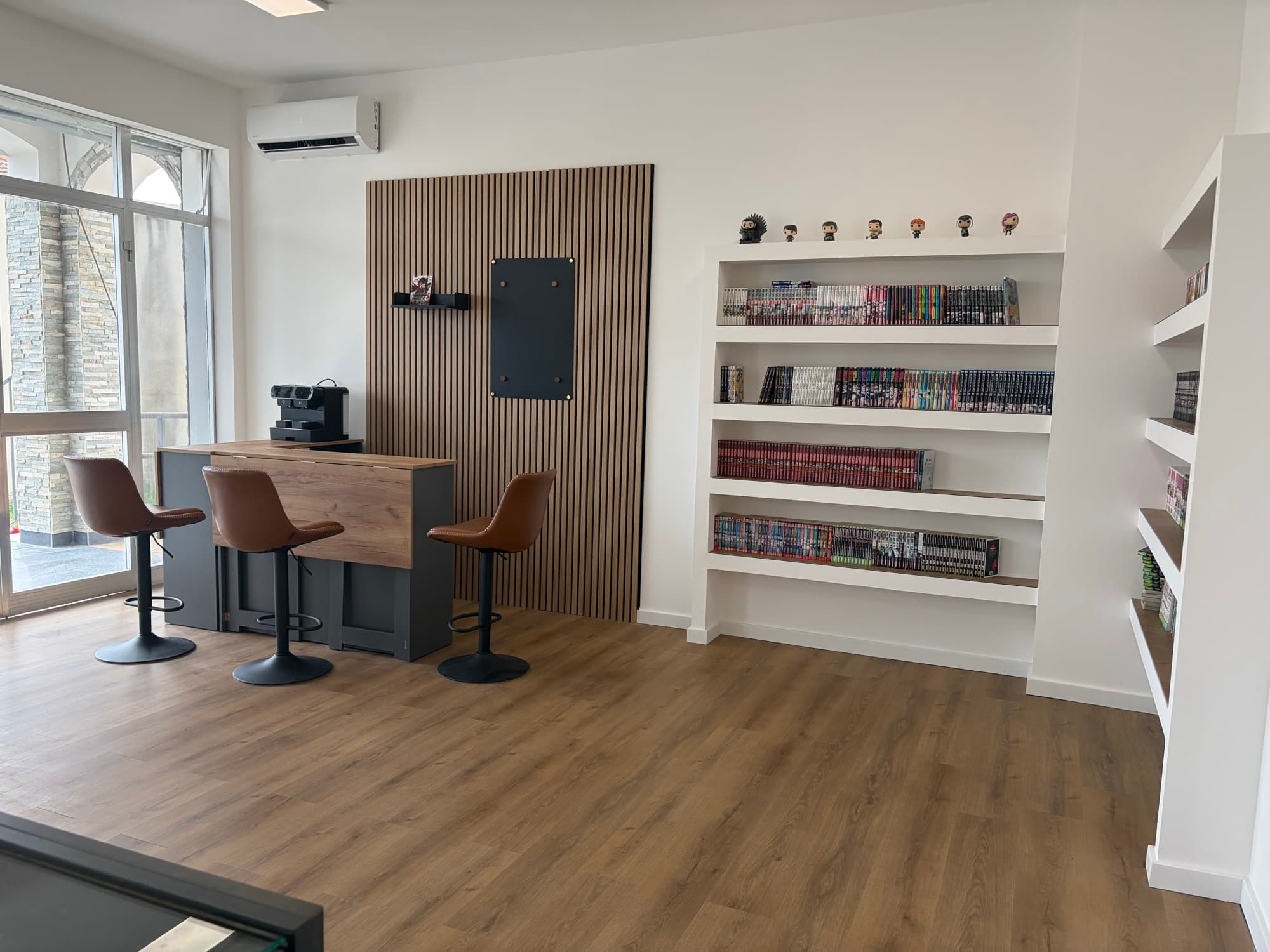 Le coin café manga : mur en tasseaux de bois, tabourets en cuir camel, machine à café